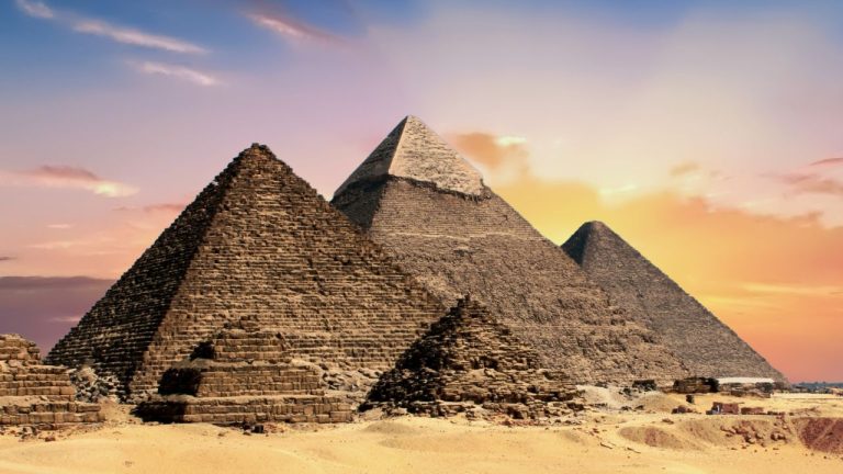 The three Great Pyramids of Giza standing against a golden sunset sky.