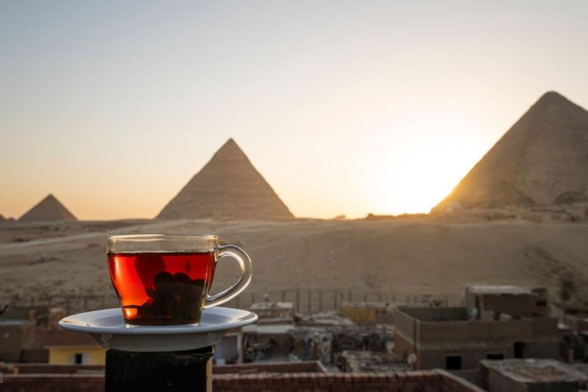 A cup of tea on a terrace overlooking the Pyramids of Giza at sunset with a golden sky in the background