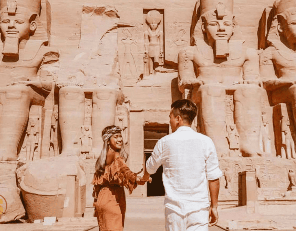A couple exploring the majestic Abu Simbel Temple in Egypt, holding hands against the backdrop of towering statues of Pharaoh Ramses II.