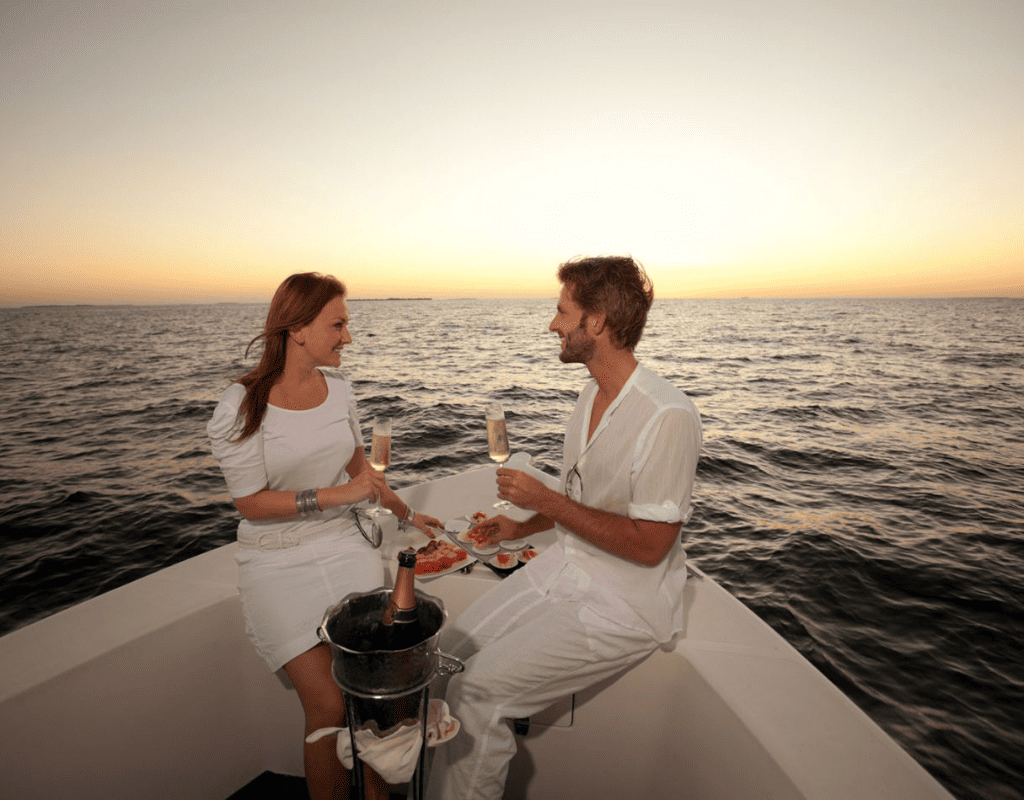 A couple enjoying a romantic dinner with champagne on a boat at sunset, surrounded by the open sea.