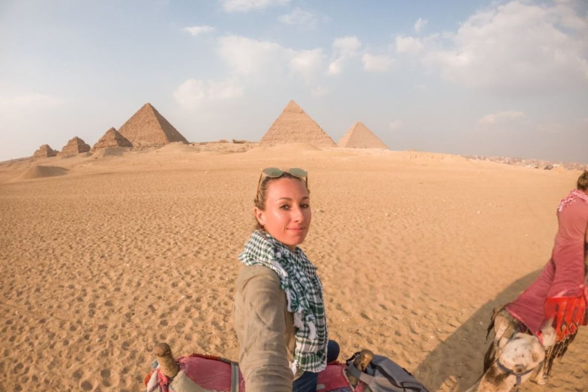 An explorer standing in front of the Pyramids of Giza admiring the ancient wonders under a clear blue sky