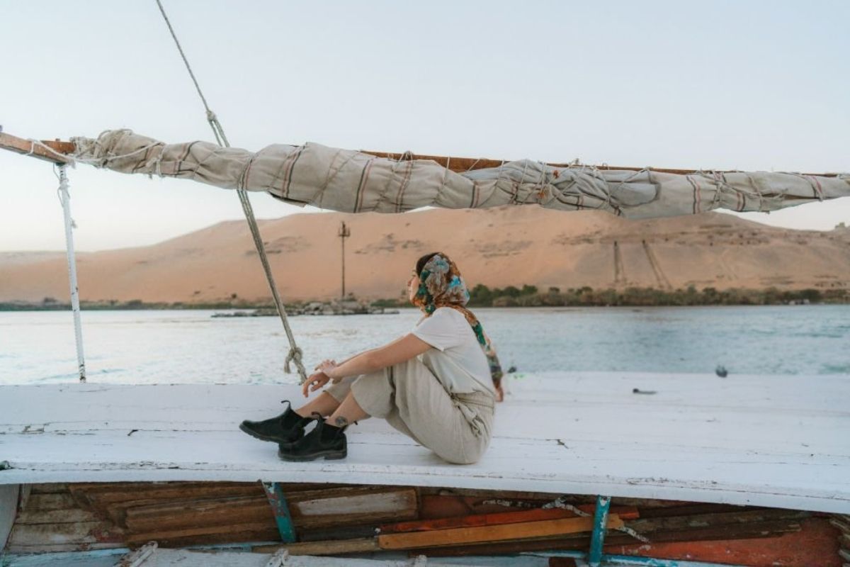 A traditional felucca sailing on the Nile River with white sails against the backdrop of a golden sunset